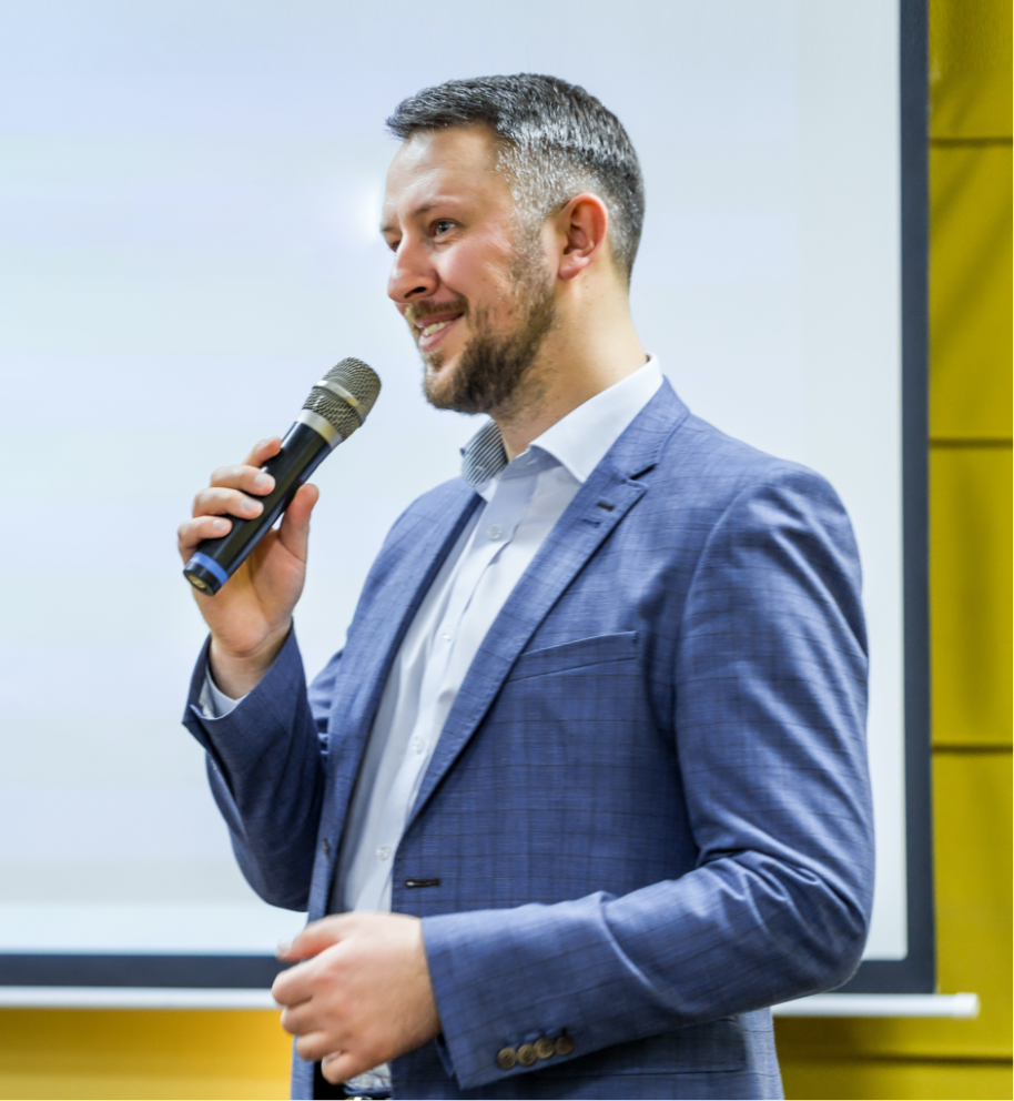 Man in a suit speaking into a microphone at a seminar