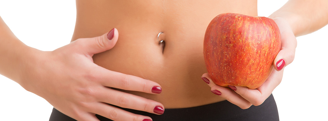 Woman holding an apple with a hand on her abdomen. Focus on the apple.