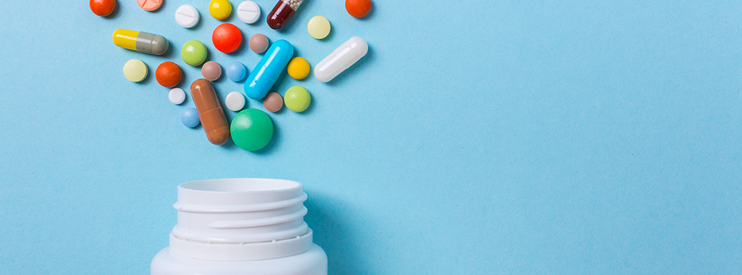 Assorted pharmaceutical medicine pills, tablets and capsules and a bottle on a blue background.