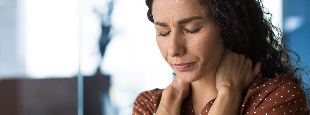 Woman grabs the back of her neck with her eyes closed as she winces in pain from a musculoskeletal condition.