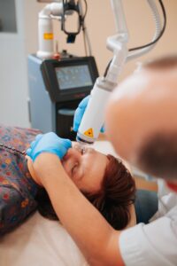 Patient receiving low-level laser therapy for skin rejuvenation during a clinical treatment session, with a clinician applying a laser device to the facial area