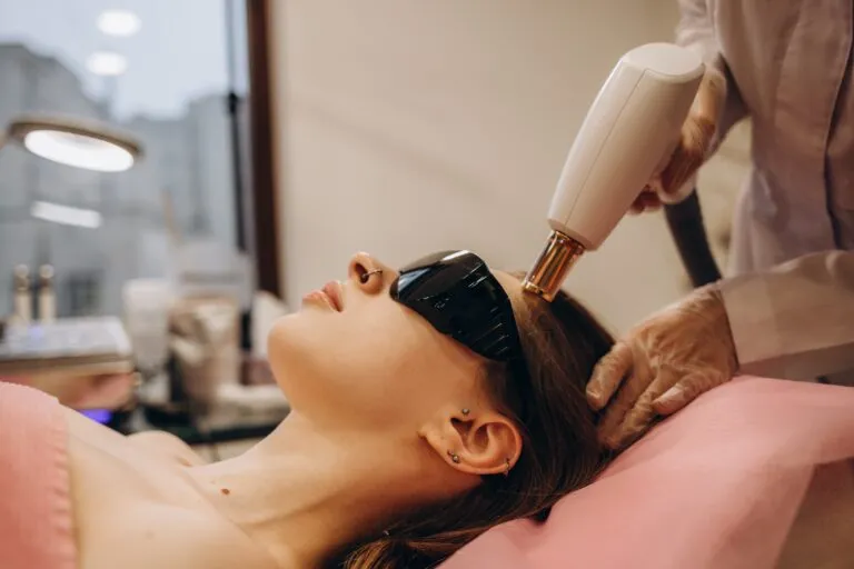 Woman in protective goggles receiving a handheld laser hair treatment to her scalp