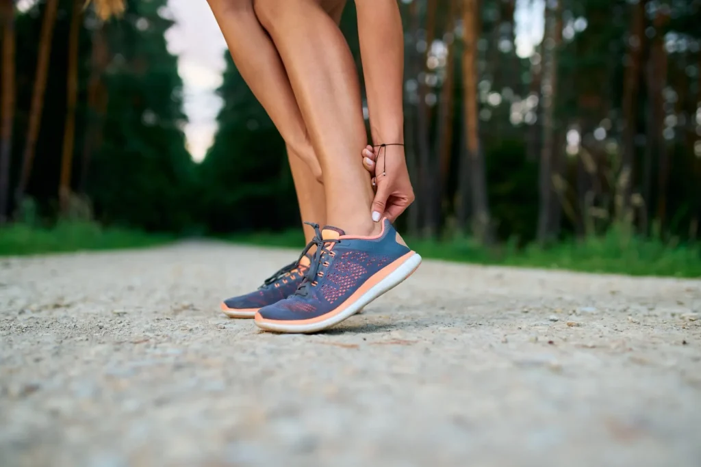 runner on a forest trail holding a painful ankle, a common sign of Achilles tendonitis