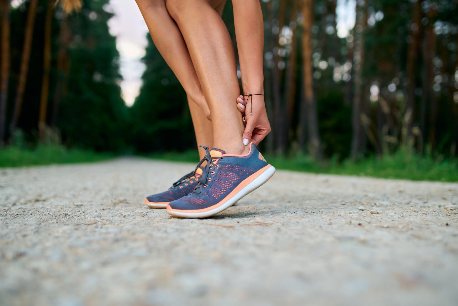 unner on a forest trail holding a painful ankle, a common sign of Achilles tendonitis