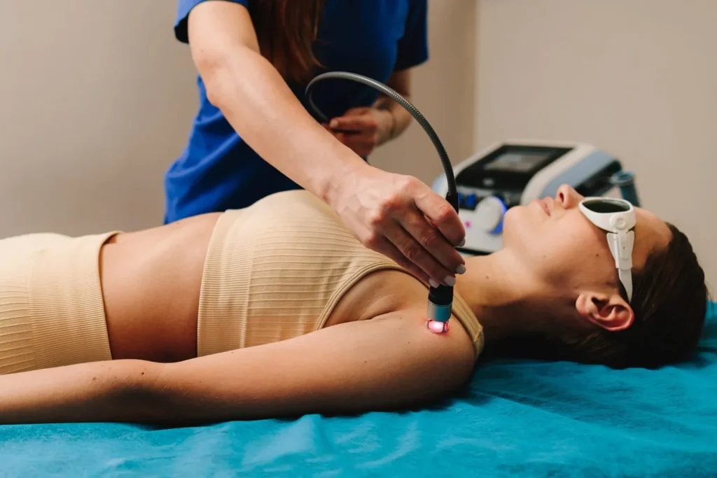 Patient wearing protective eyewear receives cold laser therapy to the shoulder during a first treatment session